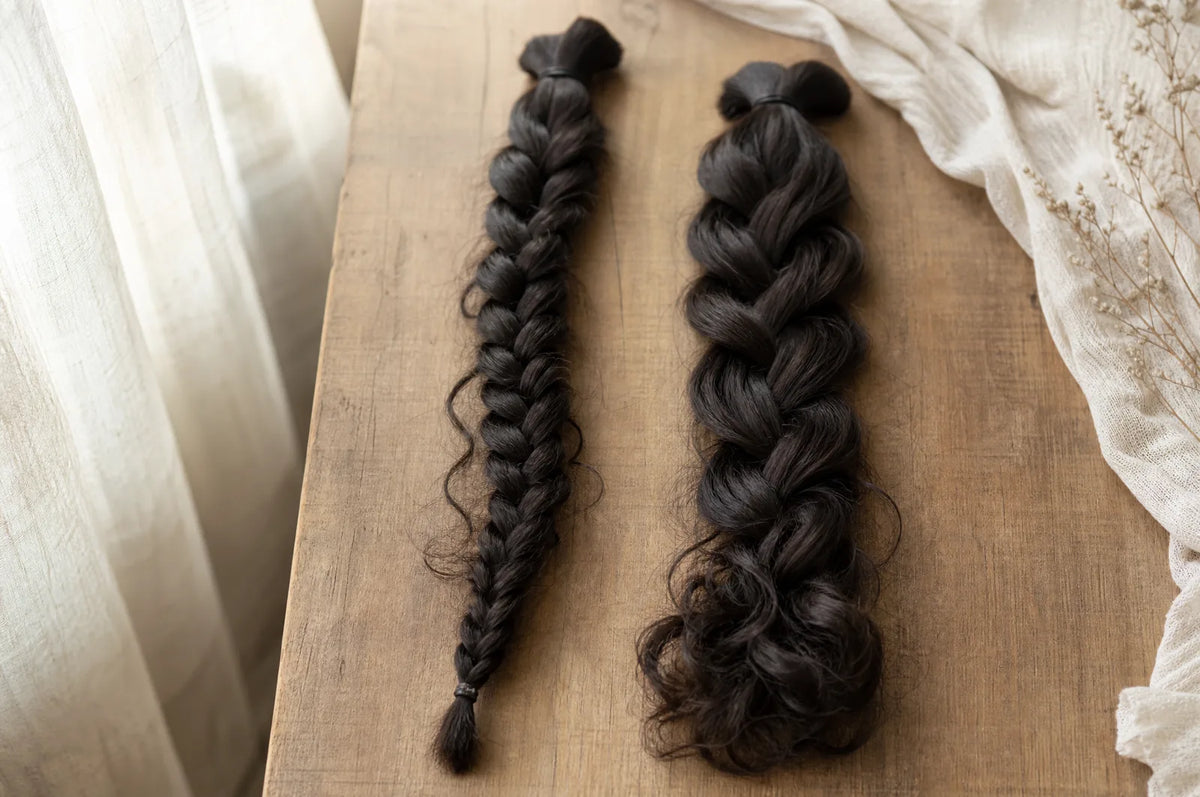 Two braided hair bundles side by side on a warm surface, one braided to the tip and one left loose with curl at the end.