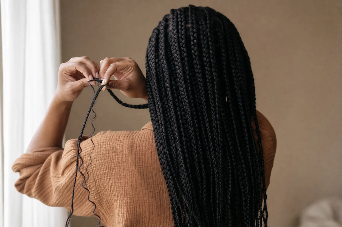 Hands unravelling the end of a dark braid against a plain warm background.